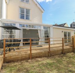 A wooden deck with a table and chairs and an umbrella outside a house with large windows and doors at Castle at The Hideaway in Tenby