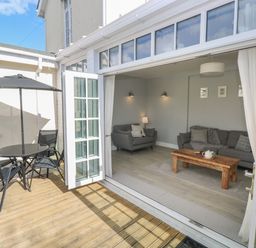 An open patio door showing a living room with sofas and a wooden coffee table and an outdoor seating area with a round table and umbrella at Castle at The Hideaway in Tenby