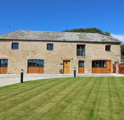 A stone building with wooden doors and windows a grass lawn and paved driveway at Mill House Boskensoe Barns in Mawnan Smith near Falmouth