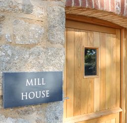 A wooden door with a small window next to a stone wall with a sign that reads mill house at Mill House Boskensoe Barns in Mawnan Smith near Falmouth