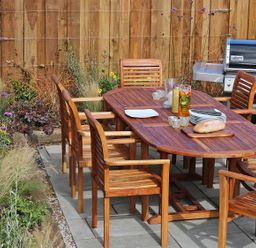A wooden outdoor dining table with six chairs next to a barbecue grill and garden at Mill House Boskensoe Barns Mawnan Smith near Falmouth