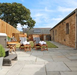 An outdoor patio with reclining wooden chairs and rolled towels next to a stone building and wooden fence at Mill House Boskensoe Barns Mawnan Smith near Falmouth