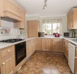 A kitchen with wooden cabinets a gas stove an oven a microwave a dishwasher and a window at The Lodge off High Street in Hadleigh