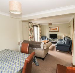 A dining table with chairs and a living room with sofas and a television at The Lodge off High Street Hadleigh