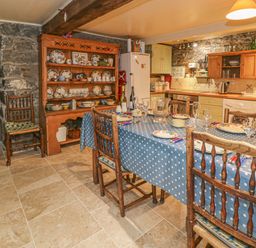 A kitchen with a dining table set with plates and glasses next to a wooden cupboard with crockery at Lower Dolgenau The Cottage in Llawryglyn near Llanidloes