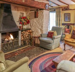 A living room with a lit fireplace wooden logs on each side different armchairs and a round rug at Lower Dolgenau The Cottage in Llawryglyn near Llanidloes