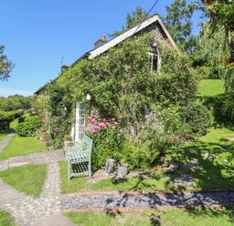 A cottage covered with climbing plants surrounded by a garden with pathways at Lower Dolgenau The Cottage in Llawryglyn near Llanidloes