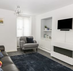 A living room with a gray armchair, a dark sofa with cushions, a wall-mounted TV, and a modern white fireplace at 11 Camden Building in Kendal