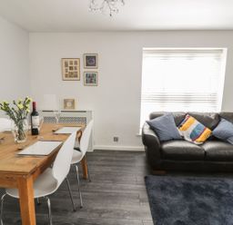 A dining table with chairs and a bottle of wine next to a sofa with cushions and a window at 11 Camden Building in Kendal