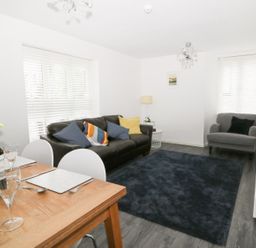 A living room with a black sofa and a gray armchair near windows with blinds at 11 Camden Building in Kendal