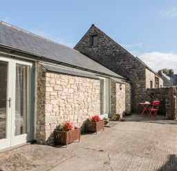 An outdoor stone patio area with flower pots and a red table and chairs set at Poppy Cottage in Llantwit Major