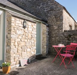 An outdoor patio with stone walls a pink table and two pink chairs at Poppy Cottage in Llantwit Major