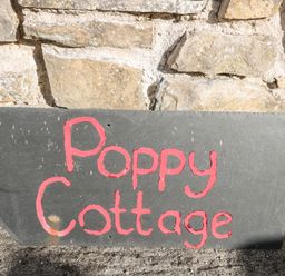 A stone wall with a black slate sign painted with red letters saying Poppy Cottage at Poppy Cottage in Llantwit Major