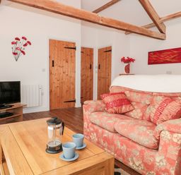 A living room with a patterned sofa coffee table tv and wooden doors at Poppy Cottage in Llantwit Major