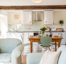 A kitchen and dining area with a wooden table, green chairs, white cabinets, and a light blue armchair at Salters Black Dog near Crediton