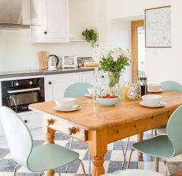 A kitchen with a wooden table set with bowls cups and a vase of flowers at Salters Black Dog near Crediton