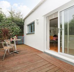 A wooden deck with two chairs and a small table with mugs outside a white house with sliding glass doors at Bolitho's Retreat in Helford