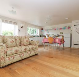 A living area with a patterned sofa a dining table with chairs and a kitchen with appliances at Bolitho's Retreat in Helford