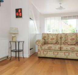 A living room with a patterned sofa a small round table with a lamp and two flower paintings on the wall at Bolitho's Retreat Helford