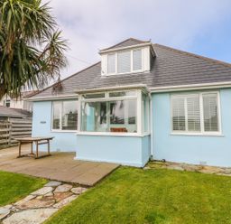 A blue house with a tiled roof and white-framed windows a wooden table patio area a palm tree and a stone pathway in the garden at Bolenowe Trebetherick near Polzeath