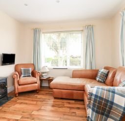A living room with a leather sofa armchair side table lamp a wall-mounted TV and a heater at Bolenowe Trebetherick near Polzeath