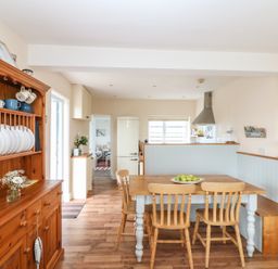 A kitchen with a wooden dining table and chairs next to a wooden cabinet with dishes at Bolenowe in Trebetherick near Polzeath