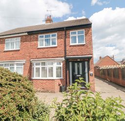 A brick semi detached house with white windows a black front door and bushes in front at Lilly May Cottage in Flamborough