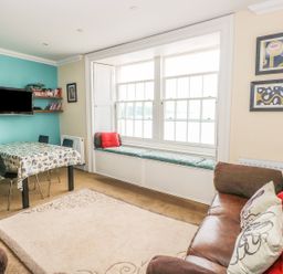 A living room with a dining table and chairs a television a window seat and a sofa with cushions at Apartment 2 in Tenby