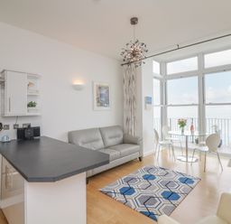 A living area with a kitchen counter sofa dining table and large windows overlooking the sea at Oceans Side in Ilfracombe