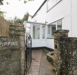 A pathway leading to a white house entrance with a glass porch behind stone walls and a black metal gate at Pippins in Bream