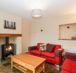 A living room with a wood burning stove red sofas a wooden coffee table and a wall niche at Pippins in Bream