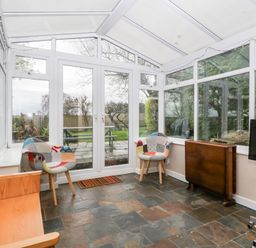 A conservatory with two patterned chairs a wooden bench a table against the wall a standing lamp and a television on a stand at Pippins in Bream