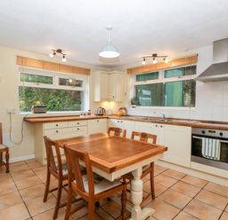 A kitchen with a wooden dining table and four chairs a stove with an oven a range hood two windows with blinds and tiled floor at Pippins in Bream