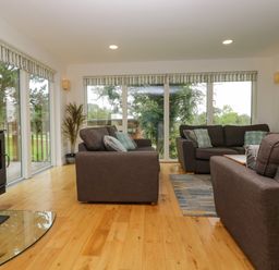 A living room with brown sofas a wood burning stove and large windows showing an outdoor view at Ash in Truro