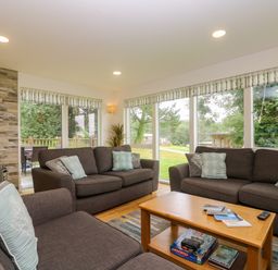 A living room with three brown sofas around a wooden coffee table with board games and books and a fireplace at Ash in Truro