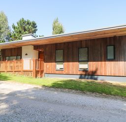 A single-story wooden house with a fenced porch and gravel driveway surrounded by grass at Ash in Truro