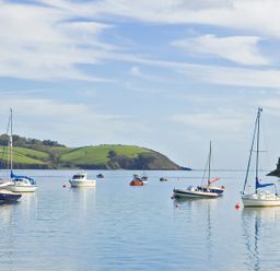 Boats floating on calm water with green hills and trees in the background at Long House Boskensoe Barns in Mawnan Smith