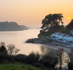 A coastal scene with houses near a beach and trees at sunset at Long House Boskensoe Barns in Mawnan Smith