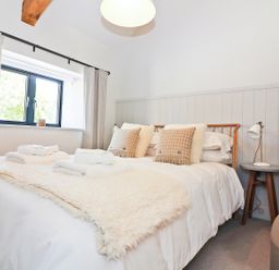 A bedroom with a bed with pillows and towels next to a window and bedside table with lamp at Long House Boskensoe Barns in Mawnan Smith