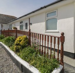 A white building with windows and doors behind a wooden railing and garden bed at Sea Spray in Dinas Dinlle