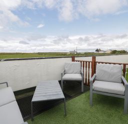 An outdoor seating area with chairs and a table on artificial grass surrounded by a white wall and wooden fence at Sea Spray in Dinas Dinlle