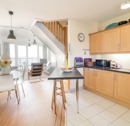 A kitchen with wooden cabinets and a dining area with a table and chairs at 12 West End Point in Pwllheli