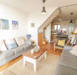 A living room with two gray sofas a wooden coffee table and an armchair next to an open kitchen at 12 West End Point in Pwllheli