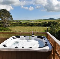 A hot tub on a wooden deck overlooking fields at Y Caban Clyd in Morfa Nefyn