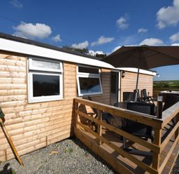 A wooden cabin with a deck patio featuring table chairs and a large umbrella at Y Caban Clyd in Morfa Nefyn
