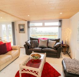 A living room with two sofas cushions a glass coffee table and a dining table with flowers at Y Caban Clyd in Morfa Nefyn