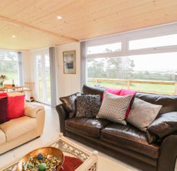 A living room with two sofas a coffee table and a dining table near large windows at Y Caban Clyd in Morfa Nefyn
