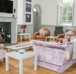 A living room with a fireplace a mounted tv brown leather armchairs and a purple sofa at Capel Bryn Bachau in Chwilog near Criccieth