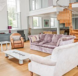A living room with sofas, armchairs, a coffee table, spiral staircase, and windows at Capel Bryn Bachau in Chwilog near Criccieth