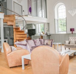 A living room with leather armchairs a purple sofa a spiral staircase and large windows at Capel Bryn Bachau Chwilog near Criccieth